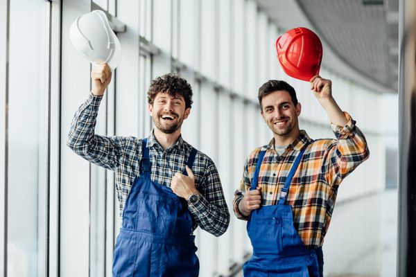Two cheerful construction workers in blue overalls and helmets